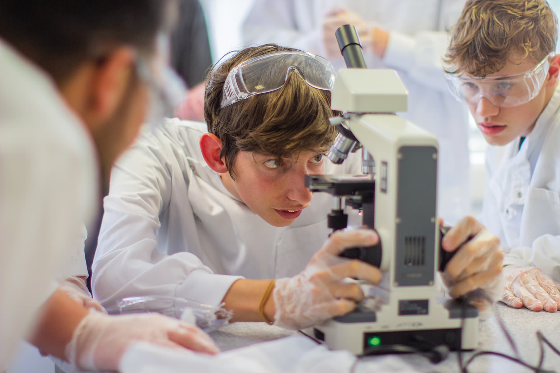 A student in a lab coat looks through a microscope during a science lesson.