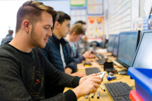 Students sit at computers in a line.