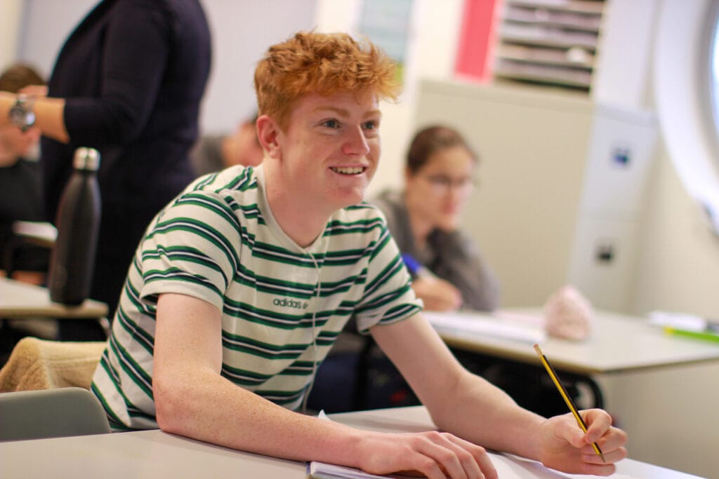 A close up of a student who is holding a pencil in a classroom.