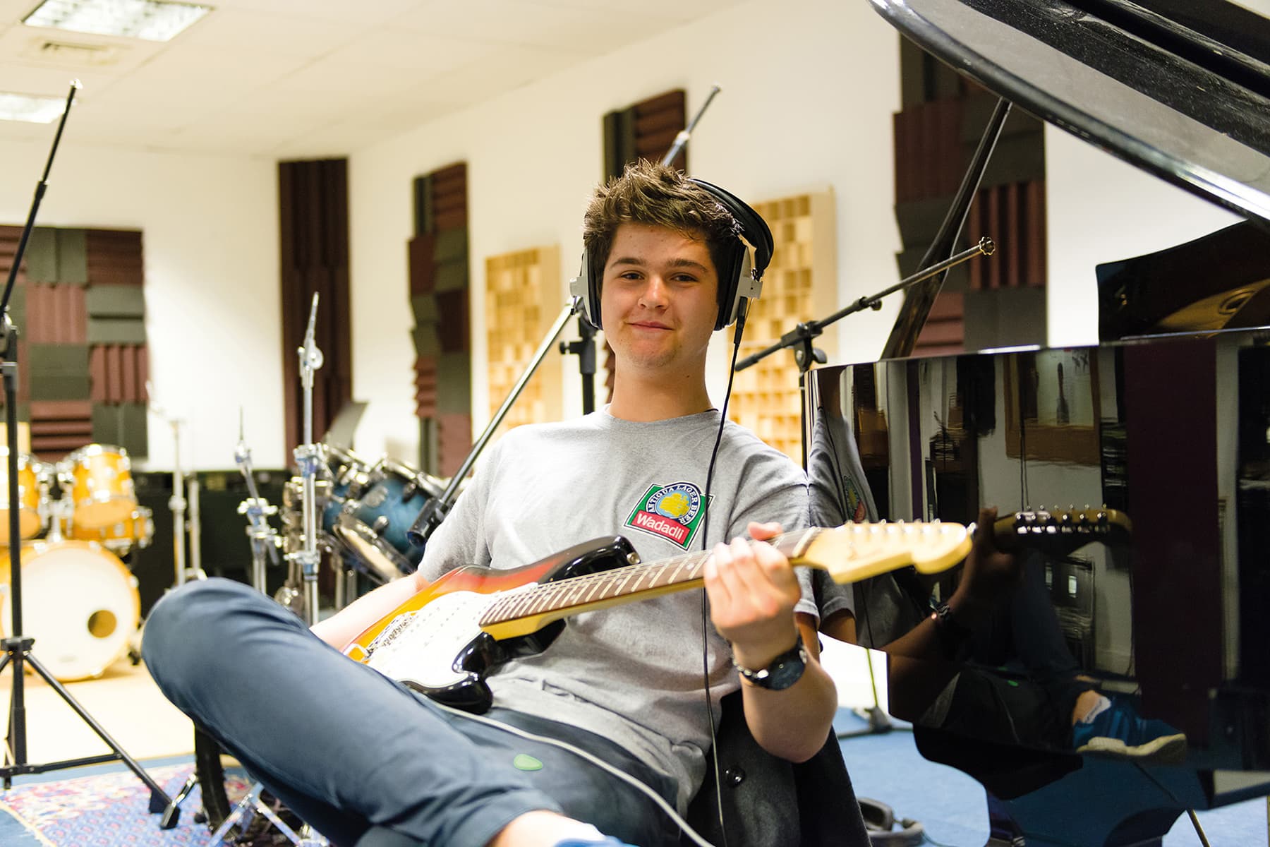 A music student sits with a guitar and a piano in the background.