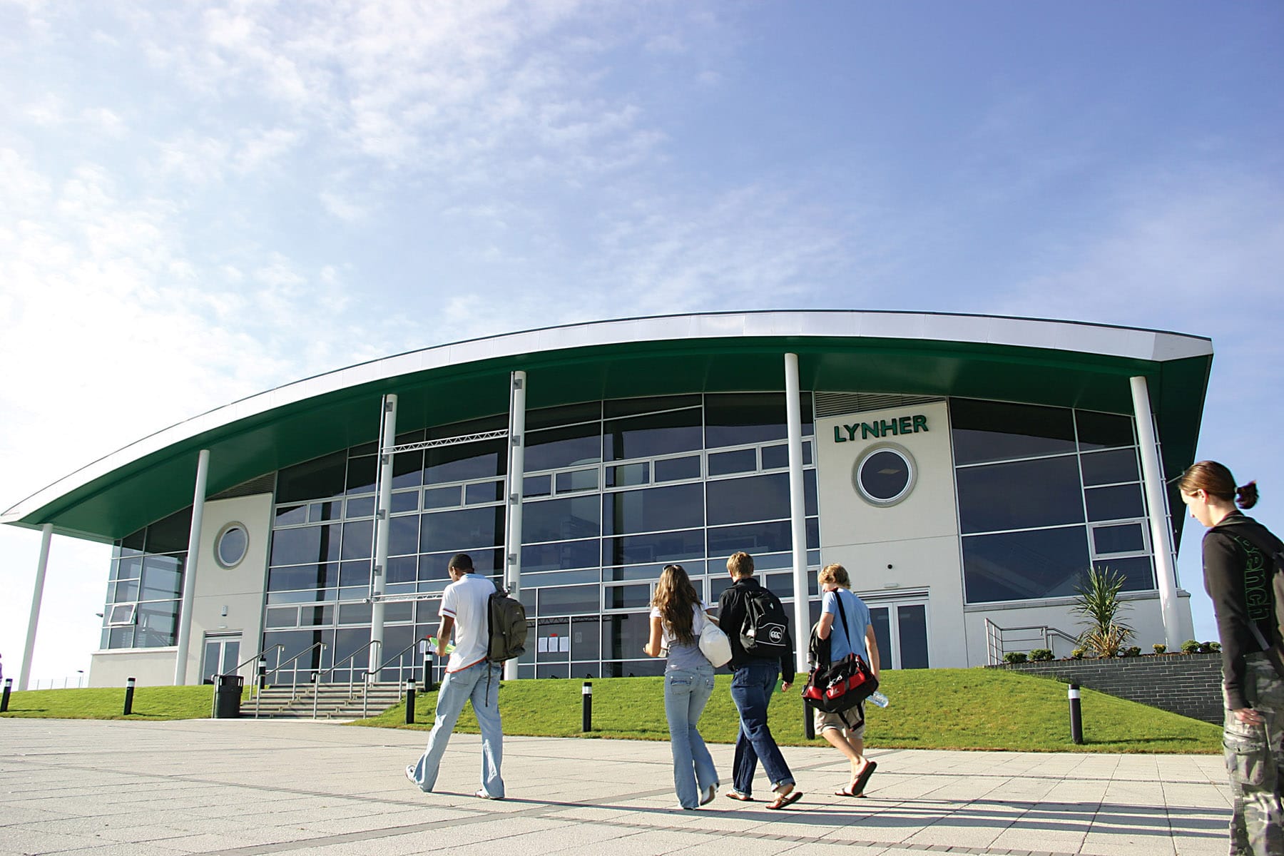 Truro College's Lynher building in the sunshine. Students are walking past, conversing with one another.