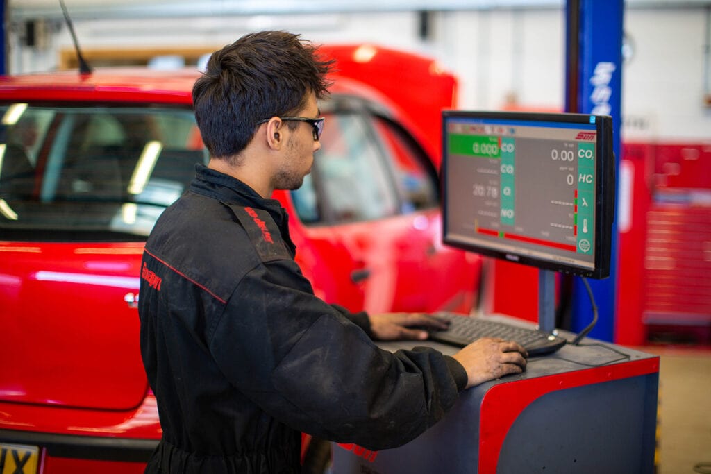 A student looks at a computer screen whilst working on a vehicle.
