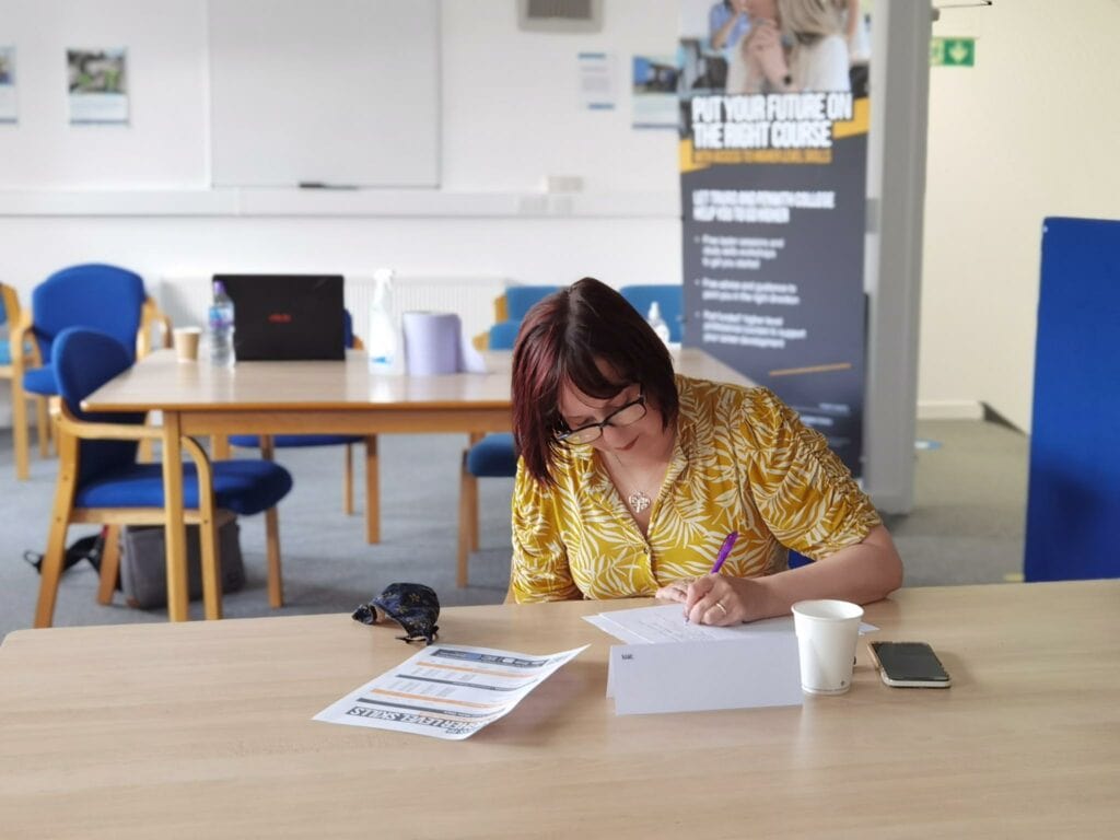 A woman sits at a table filling out paperwork with her phone and coffee cup next to her.