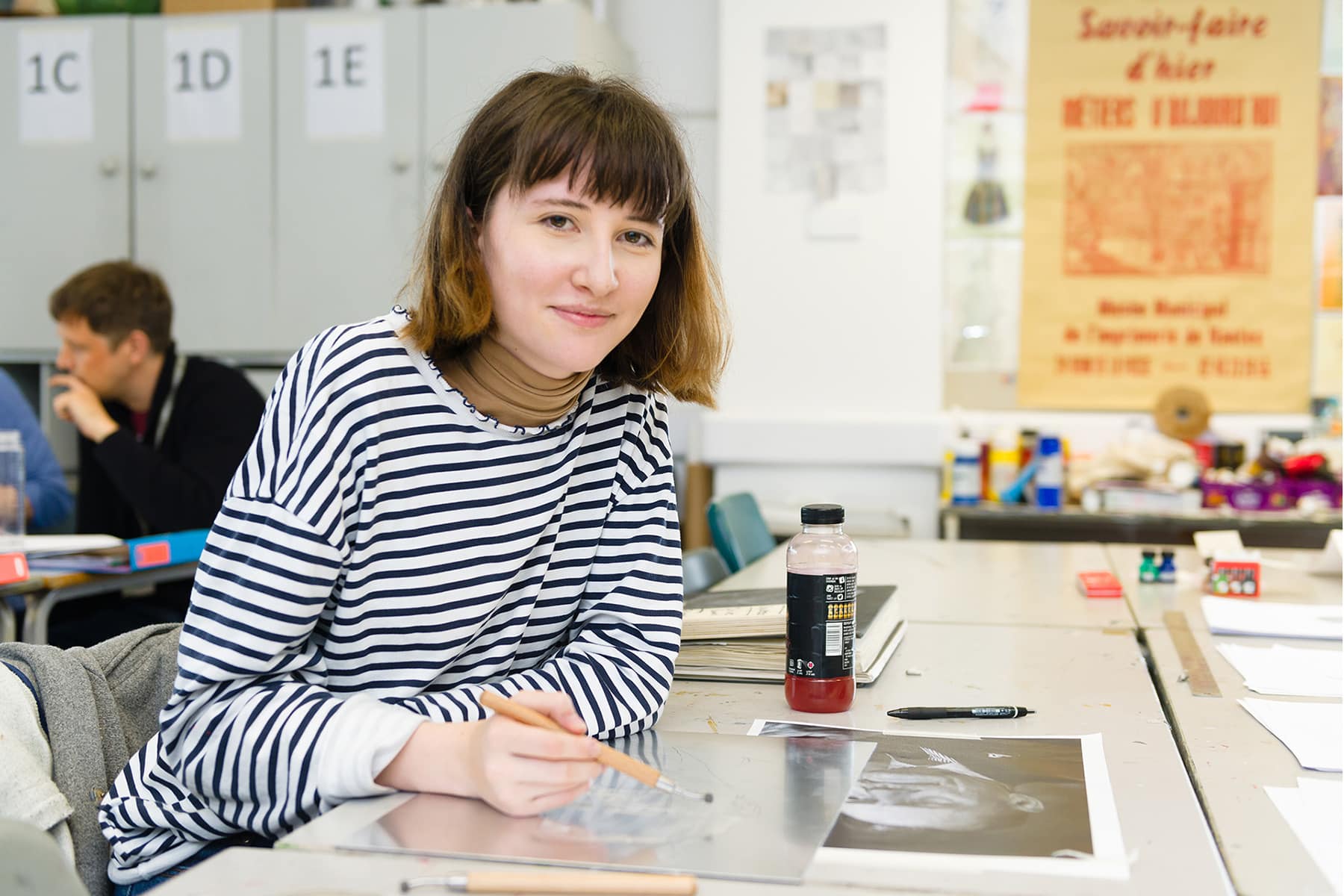 A student sits at a table in an art classroom working on some art.