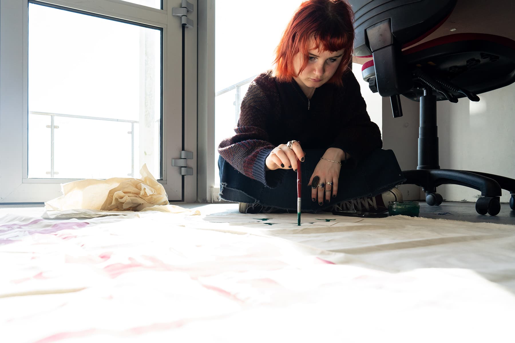 A student sits on the floor and paints onto a large piece of fabric.