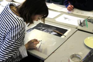 A student works on a piece of art which is spread out over a table.