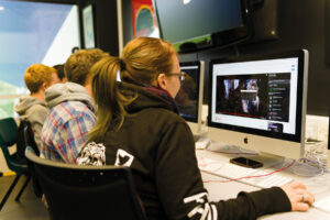 Students sit at Apple Mac computers editing videos online.