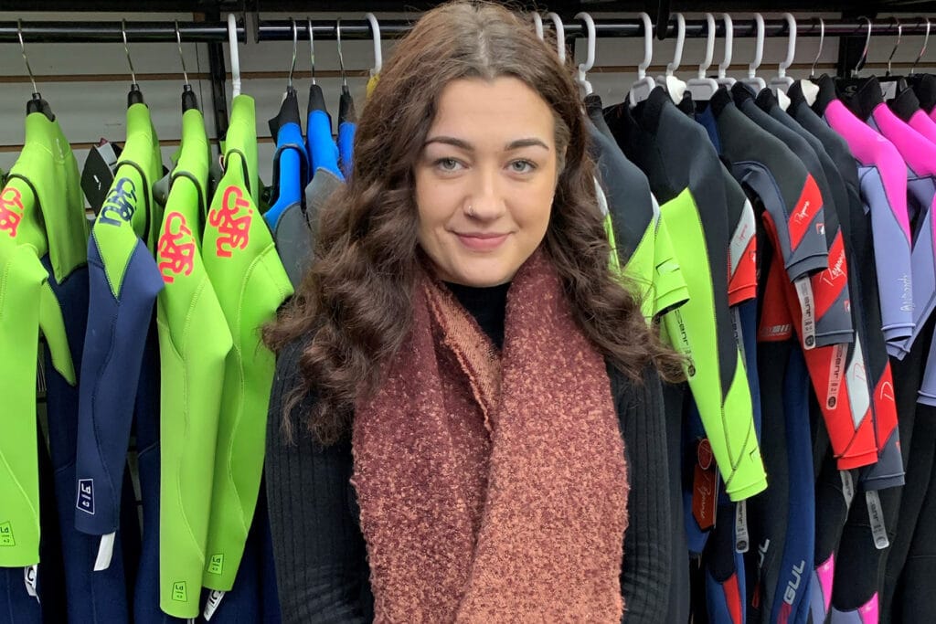 Kayleigh stood in front of wetsuits at Ann's Cottage