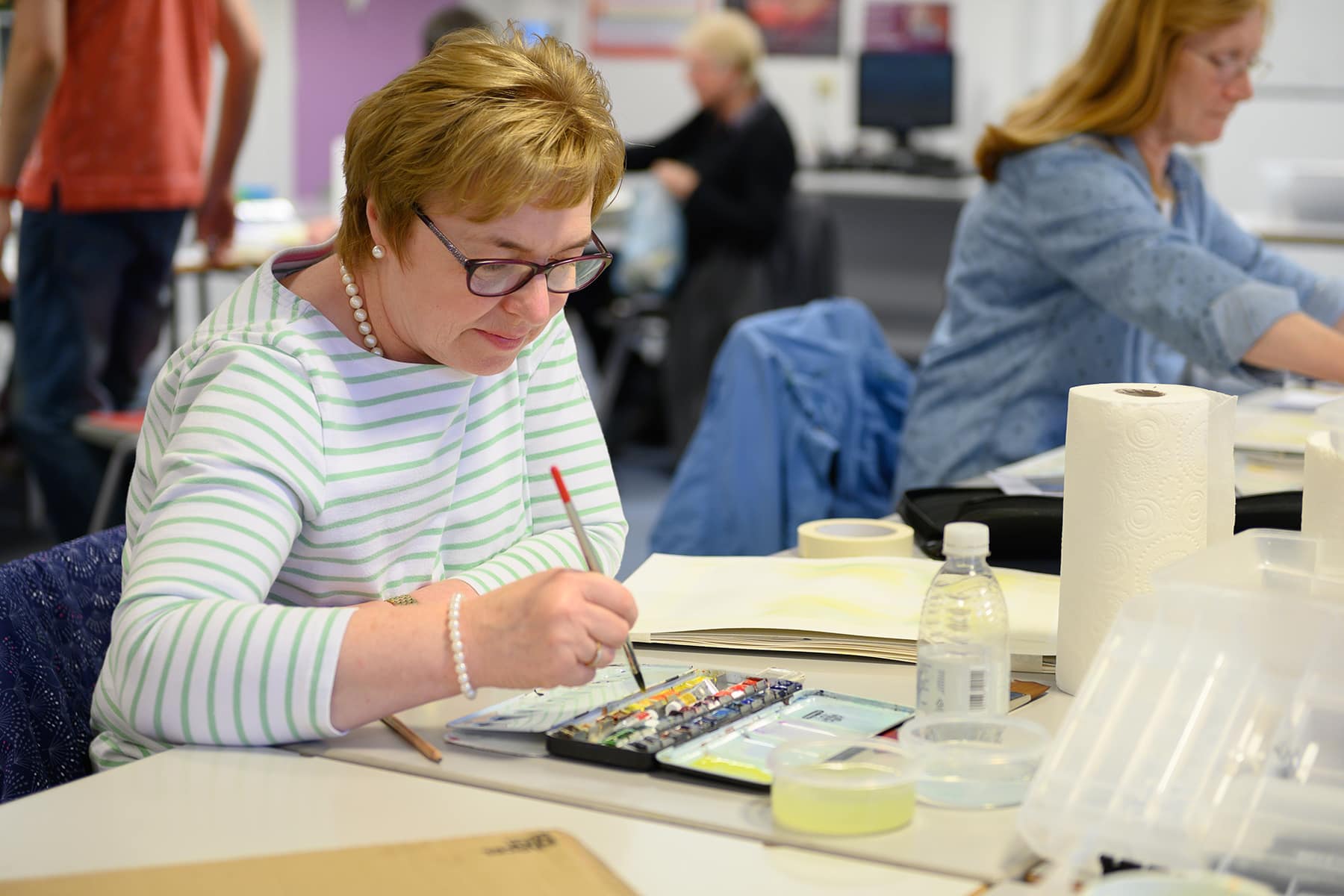 PT Art & Design A part time leisure student sits at a table with watercolours and a paintbrush.