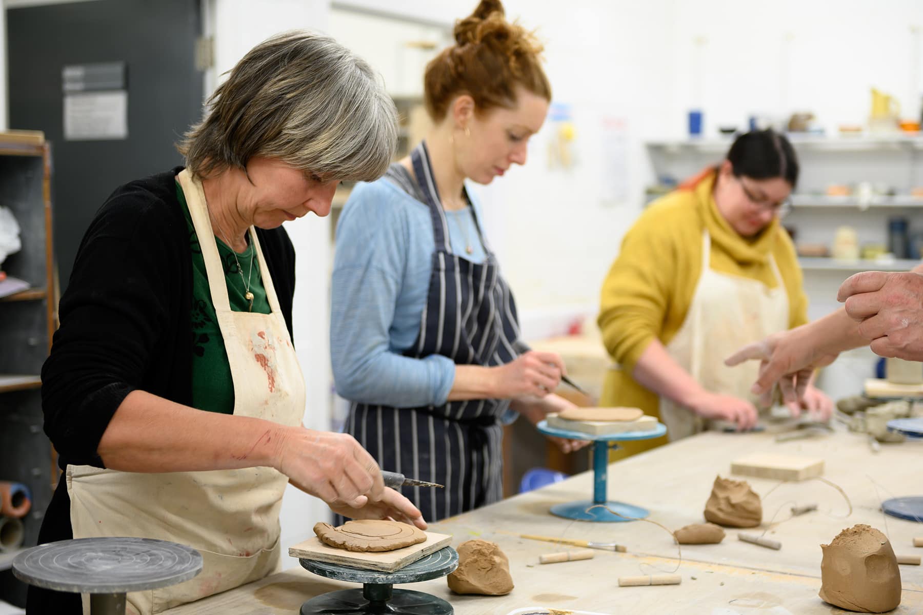 Part time leisure students in a pottery class sculpt clay on a wheel.