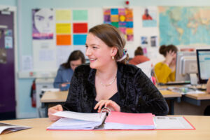 A young girl sits in a classroom with a folder open in front of her.