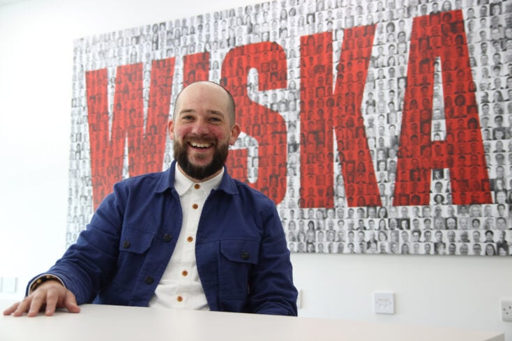 Elliott R from WISKA sat at a desk with a WISKA sign behind him