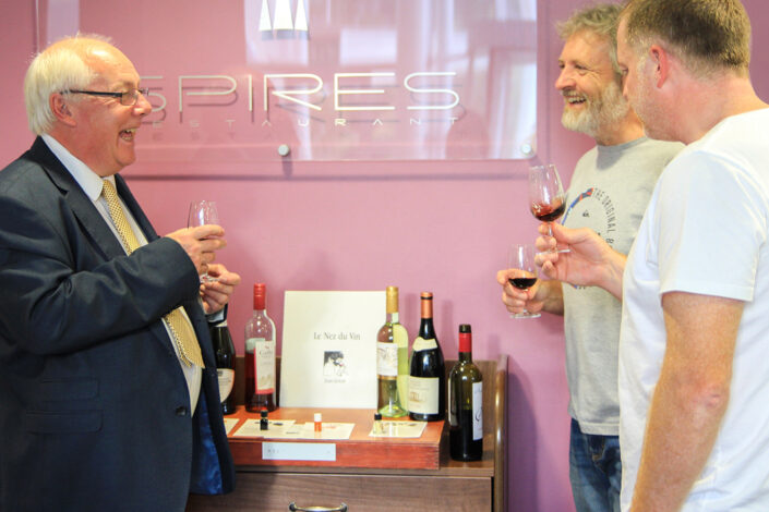 Three members of staff stand together laughing and chatting, sampling wine at a wine tasting event.