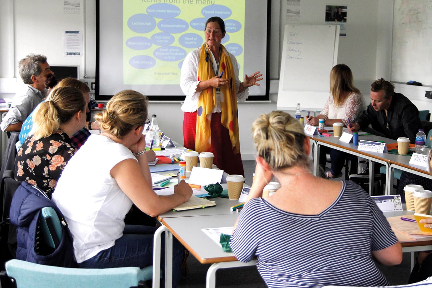 Postgraduate Certificate In Education2 A classroom of adult students watch a tutor at the front.