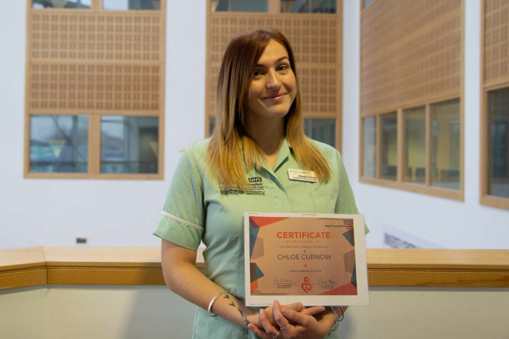 Chloe standing in her nursing uniform holding a certifcate