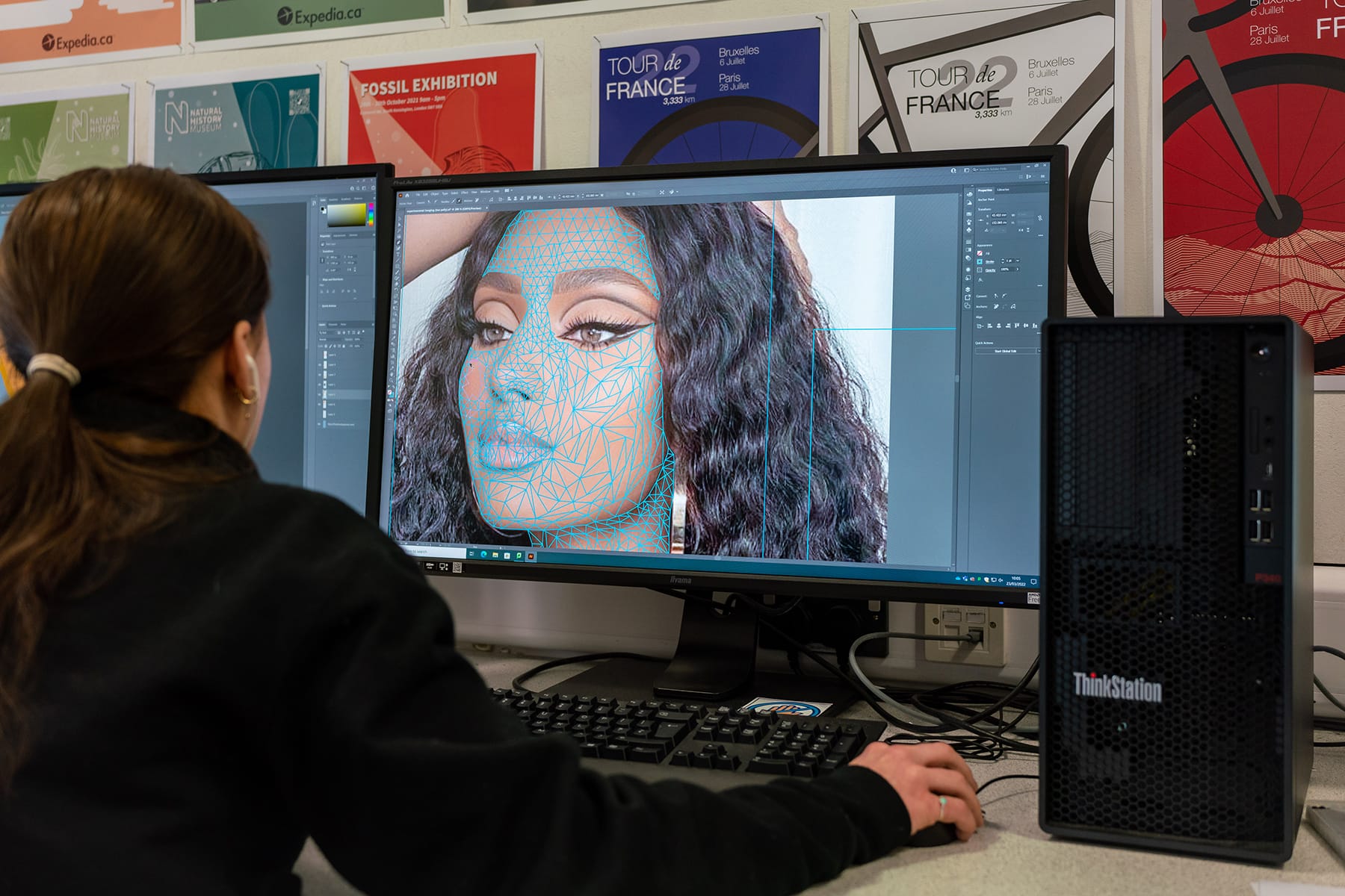 The photo looks over the shoulder of a student who is editing a photograph of a woman in photoshop.