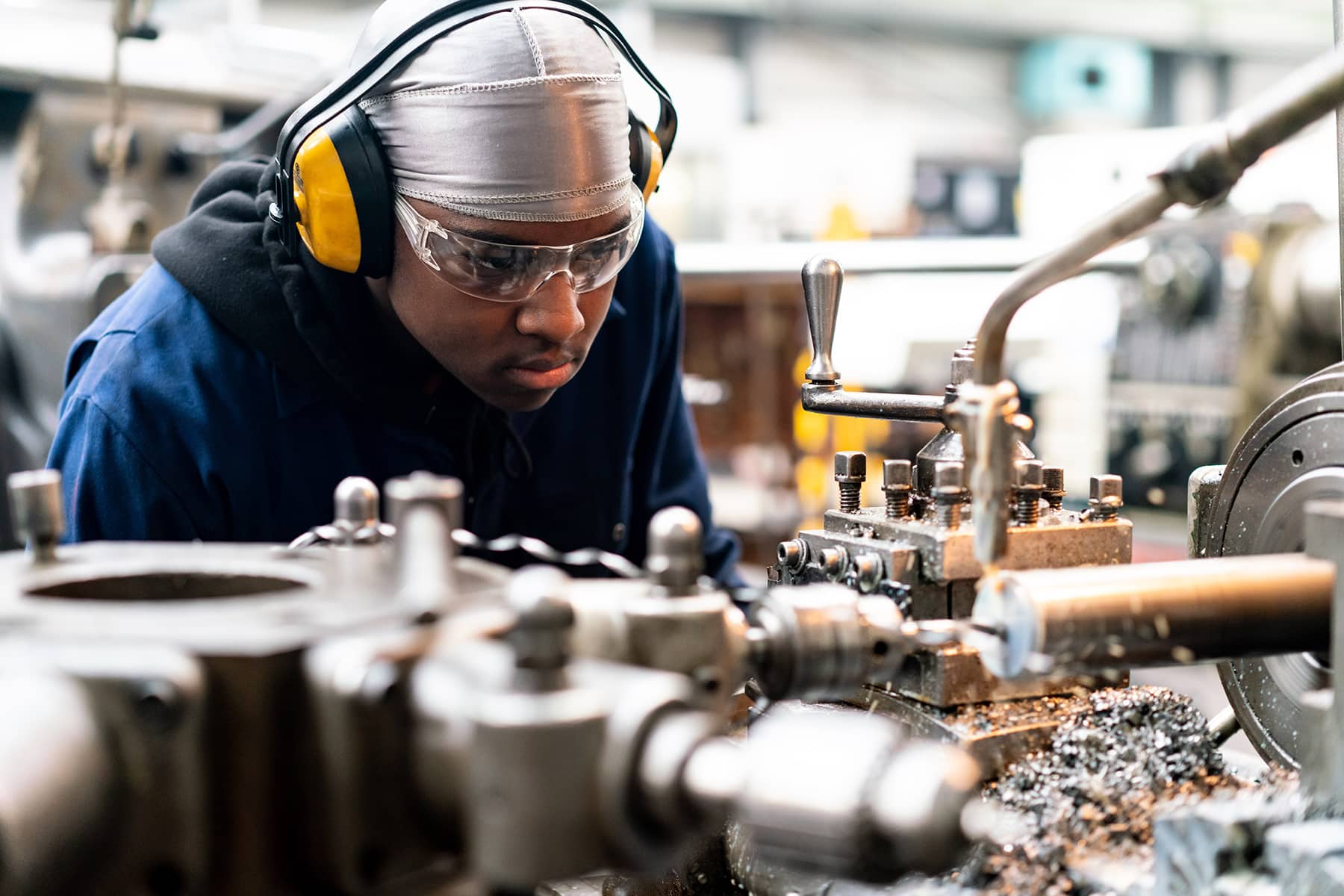 An automotive and engineering student in protective wear is looking closely at engineering machinery.