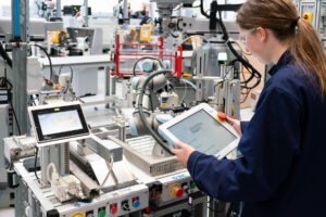 A student wearing overalls and protective eyewear looks down at engineering equipment.