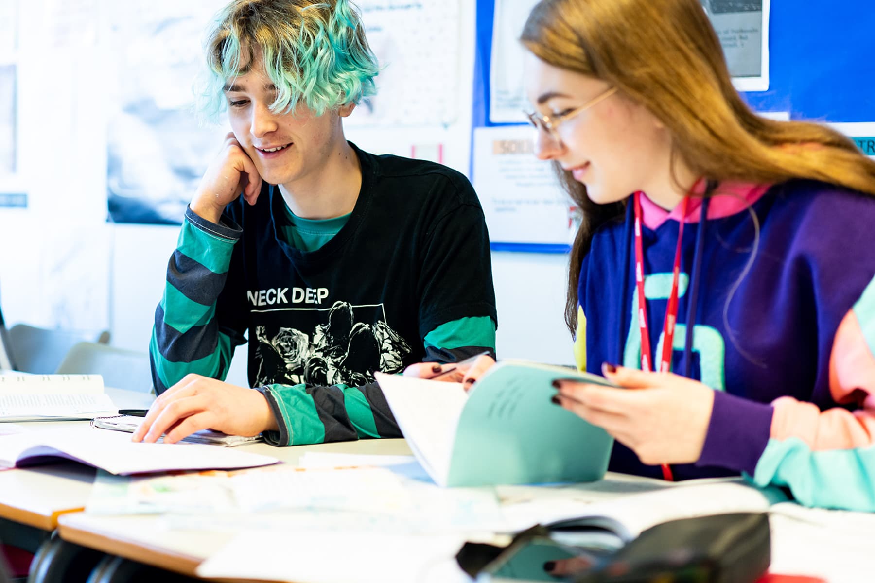 Two english and languages students sit at a desk and look through books together.