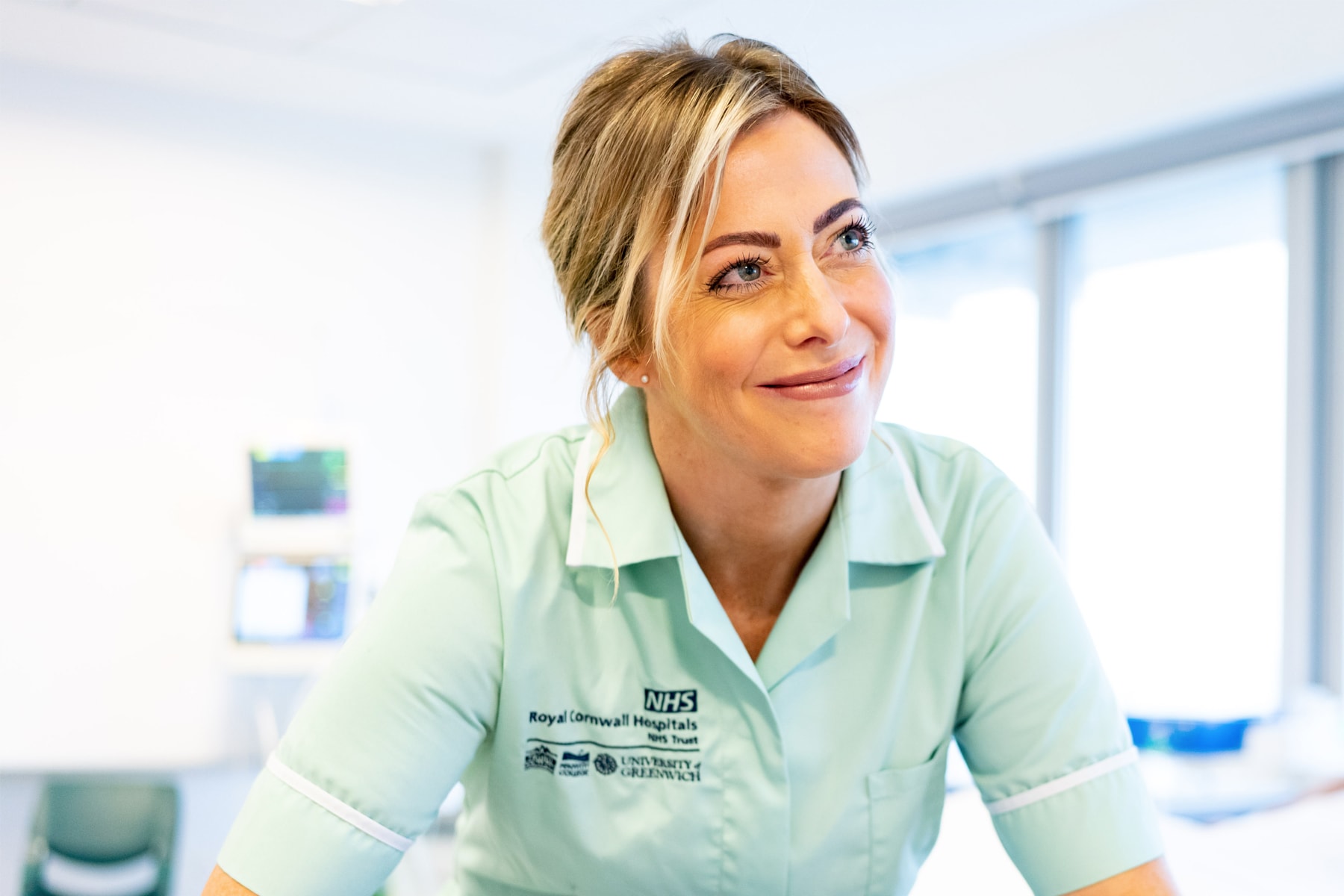 A nursing student in a green uniform looks up to the side and smiles.