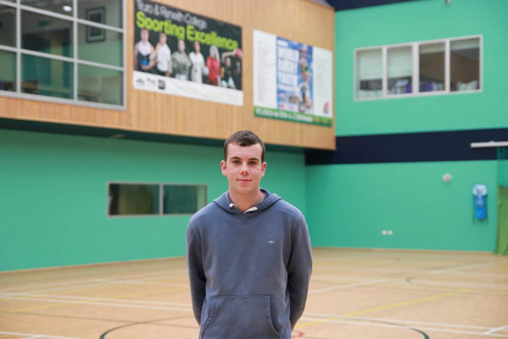 Callum is standing in the College's Sports Hall