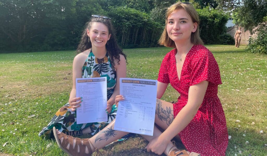 Zoe and Maddie sit on the grass with their results at Penwith College