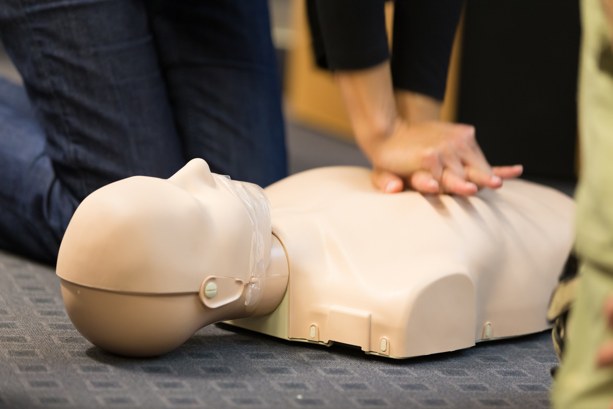 A group of adult education students practitcing CPR chest compressioon on a dummy.
