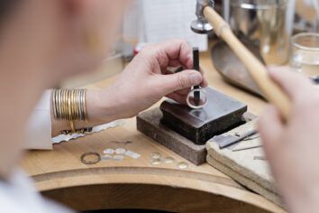 Portrait of a professional Goldsmith at work in her workshop creating a silver ring. In this picture she is stamping her hallmark on the inside on the ring. She is surrounded by the tools she uses to create her pieces of jewellery. Colour, horizontal with some copy space.