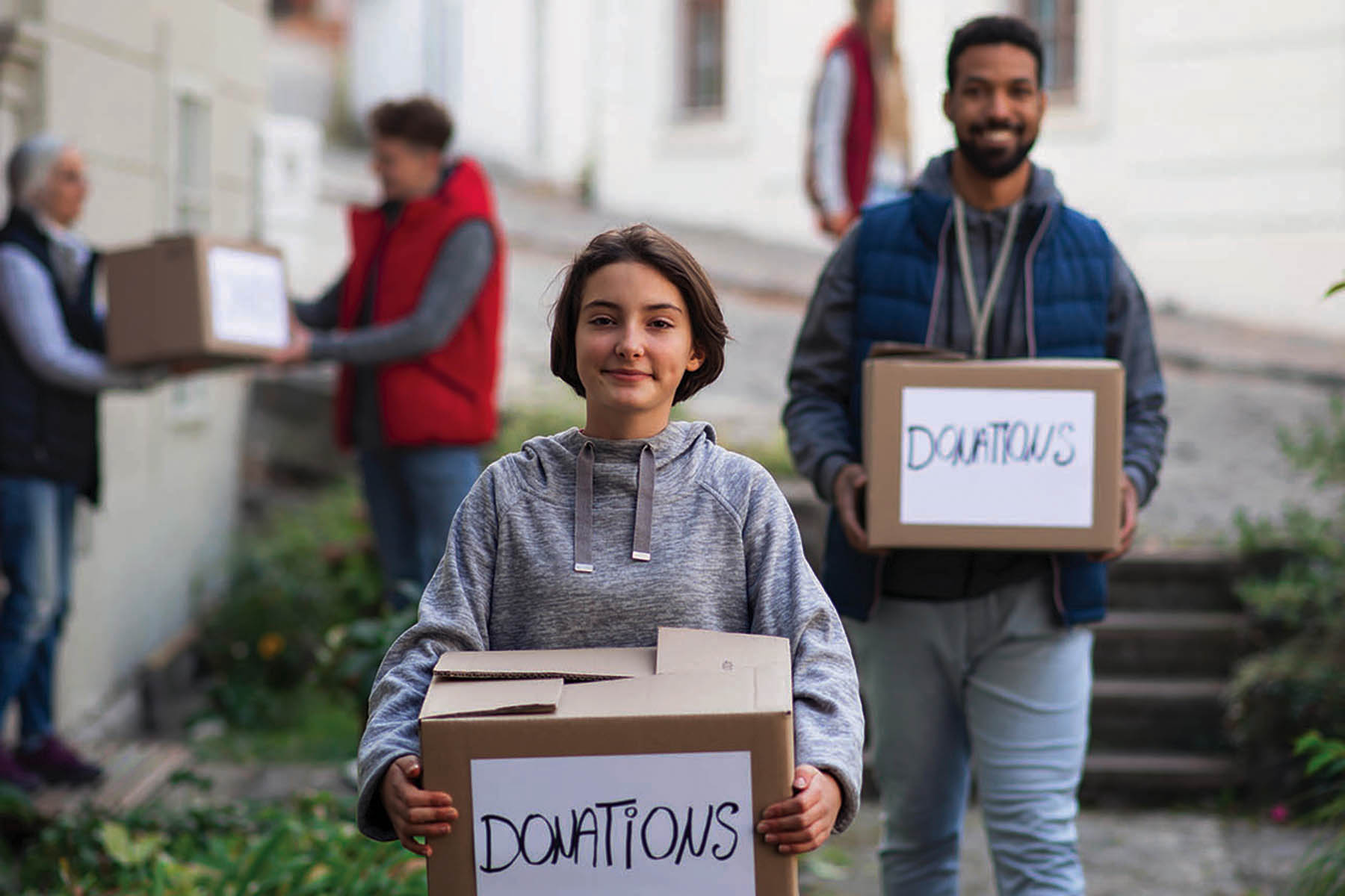 Happy preteen girl volunteer with team delivering donation boxes and looking at camera, social care concept