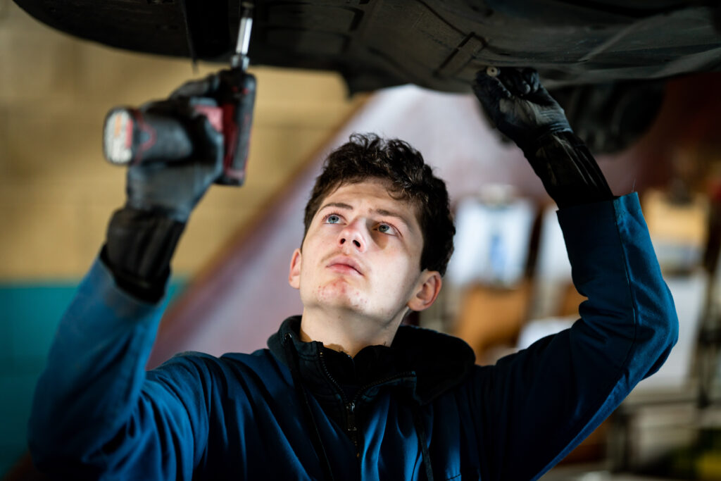 An Apprentice car mechanic working on the underside of a vehicle.