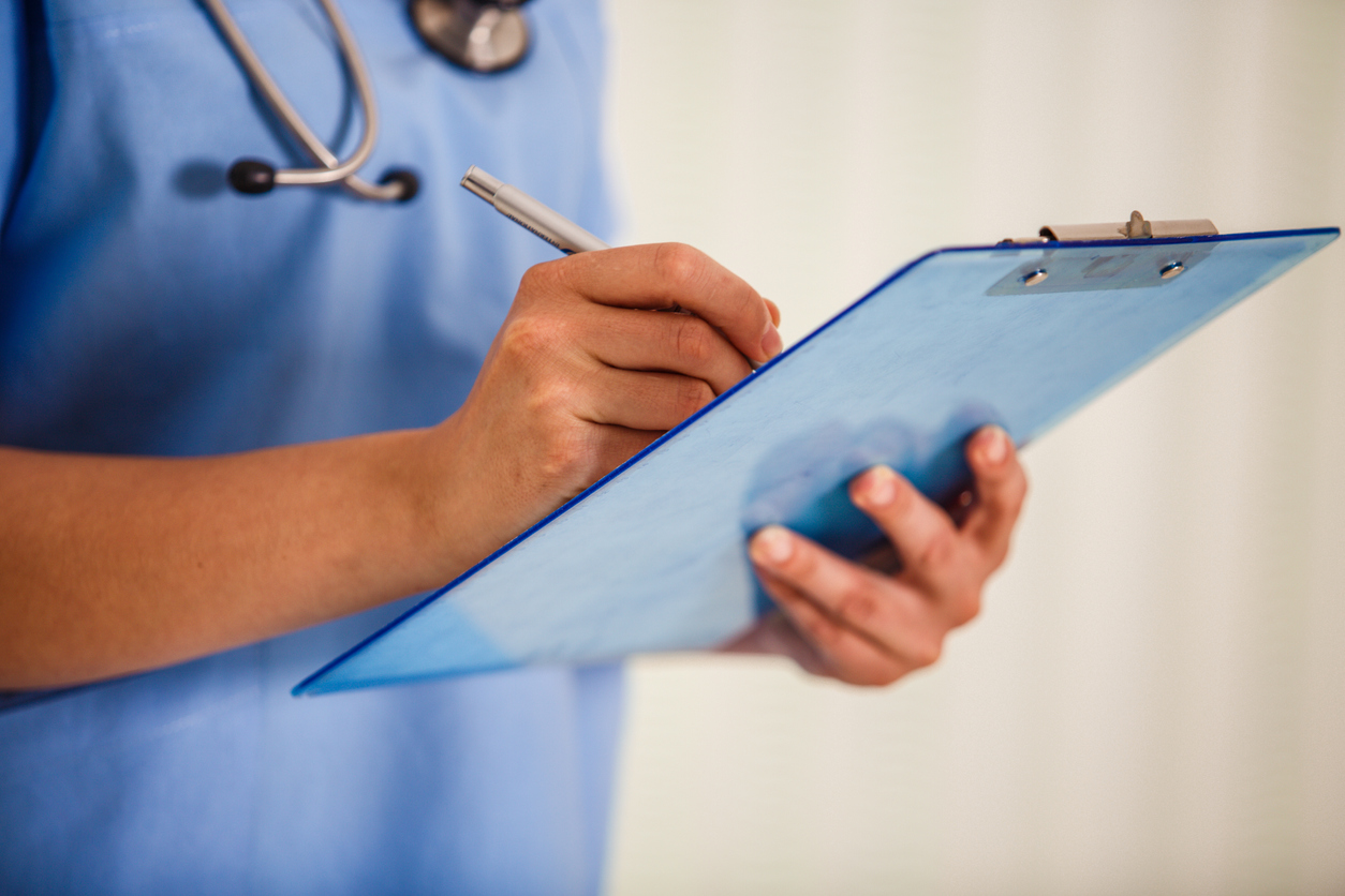 Midsection of unrecognizable female nurse holding a medical chart and writing diagnosis in it.