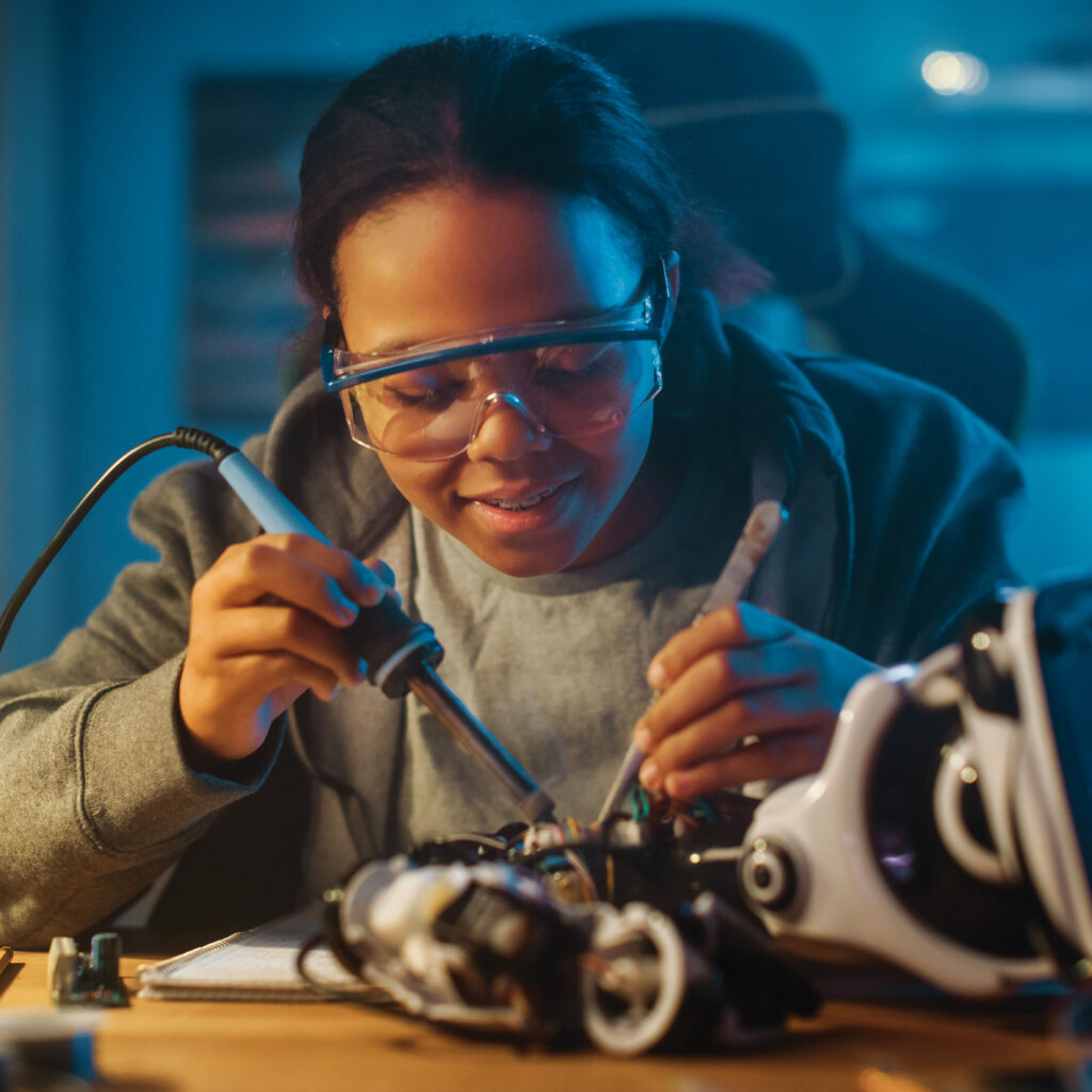 A young girl wearing goggles works on a piece of electrical equipment.