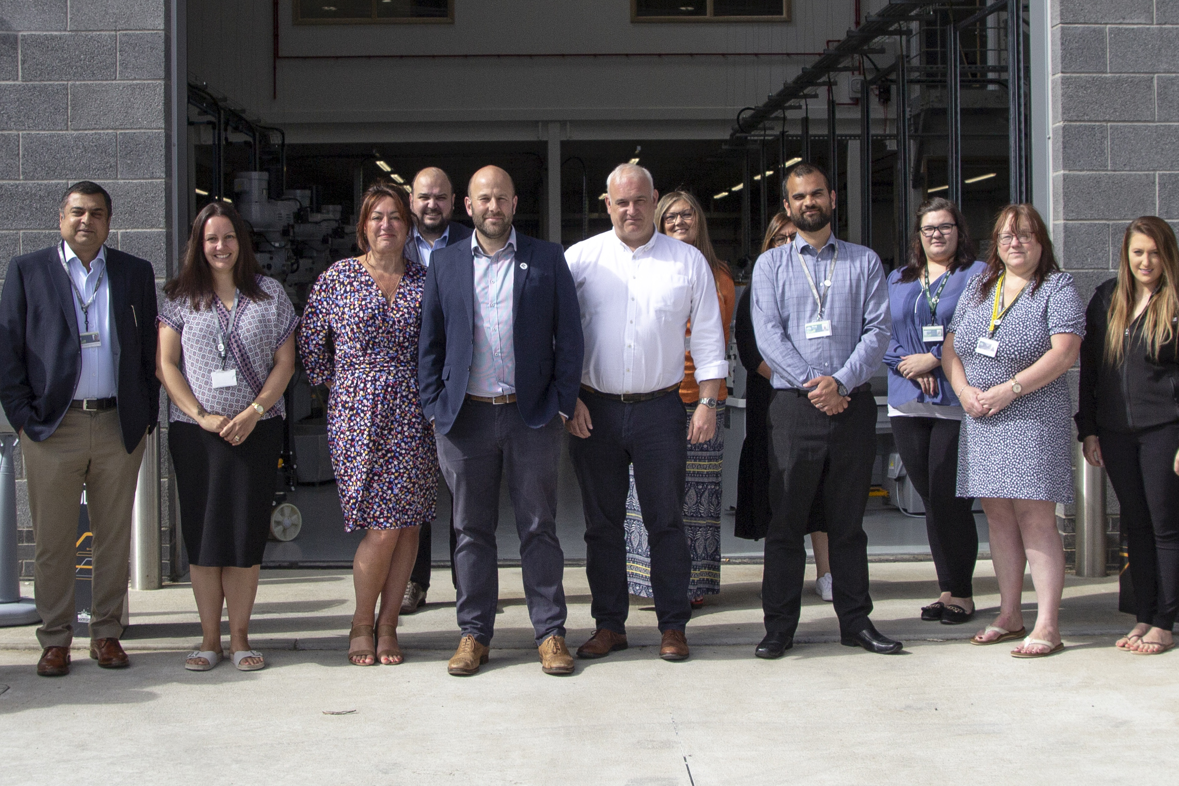 A group photo of the Business team stood outside of the Valency building. Everyone faces the camera and smiles.