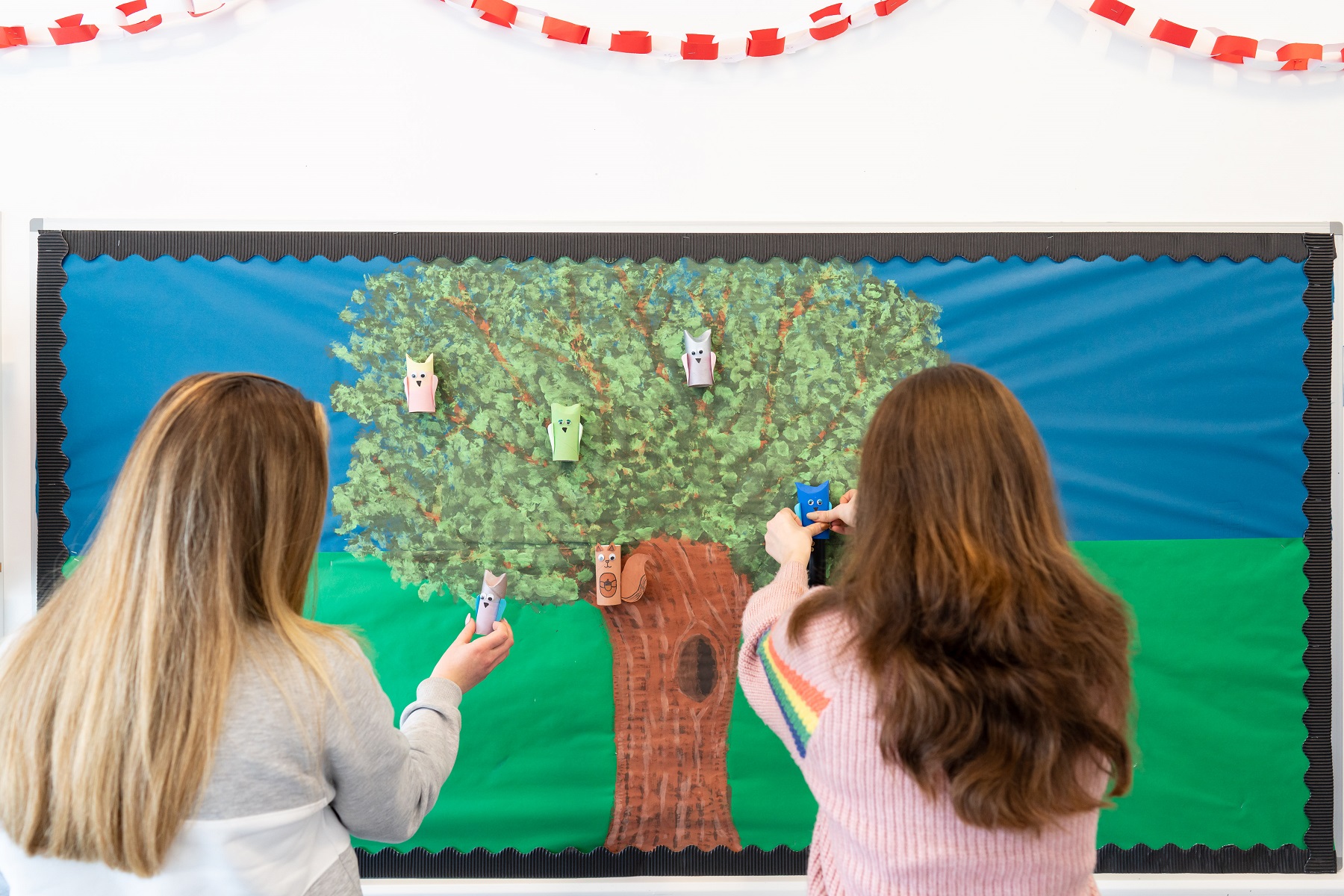 View over the shoulder of two students who are pinning crafts to a school noticeboard