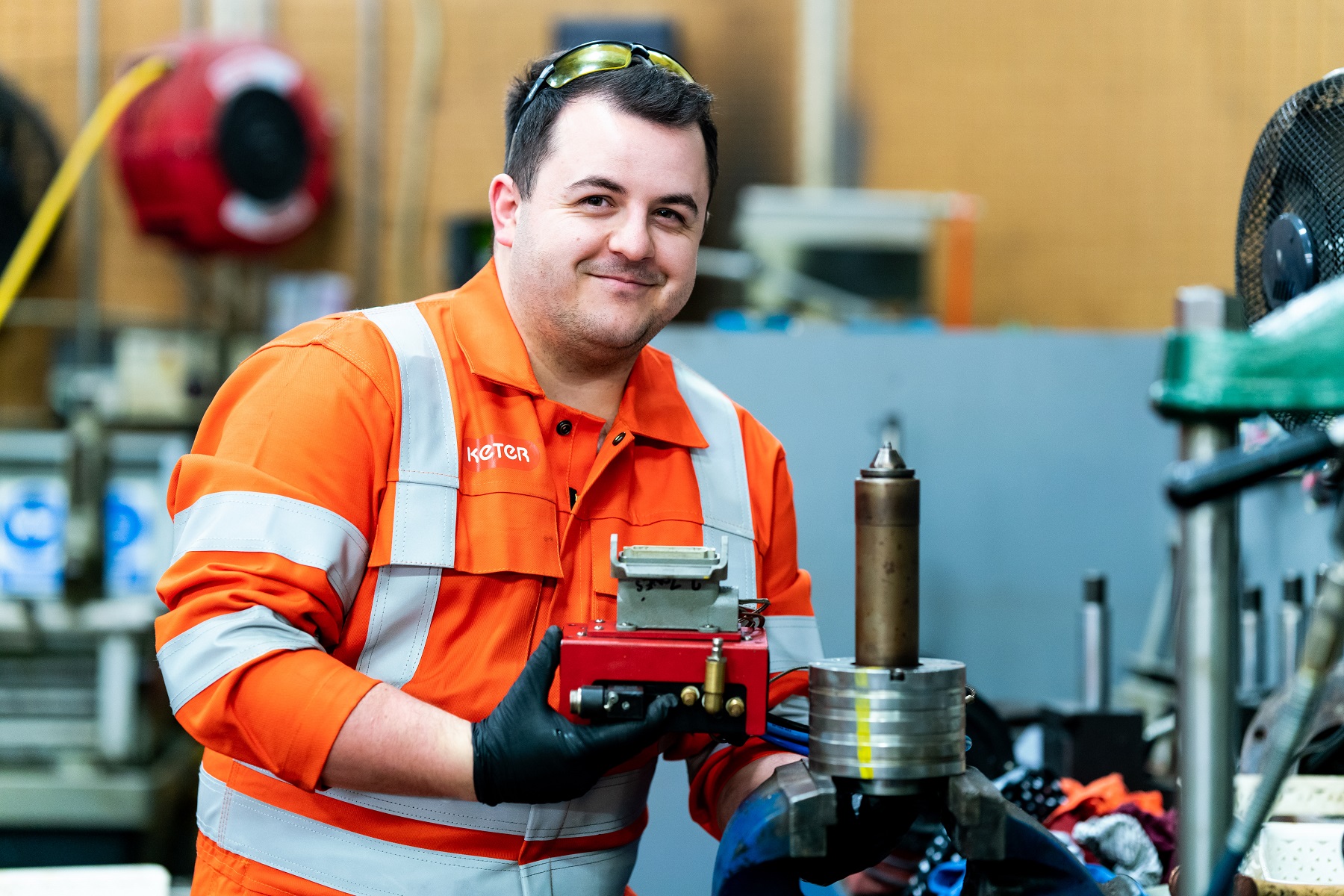 A young man in high vis overalls smiles at the camera as he works with engineering equipment.