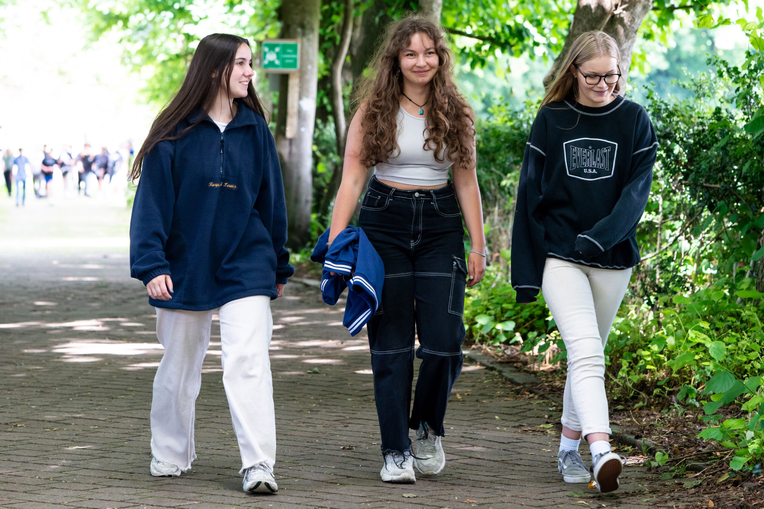 An image of three students walking down a lane. There are more students in the background.