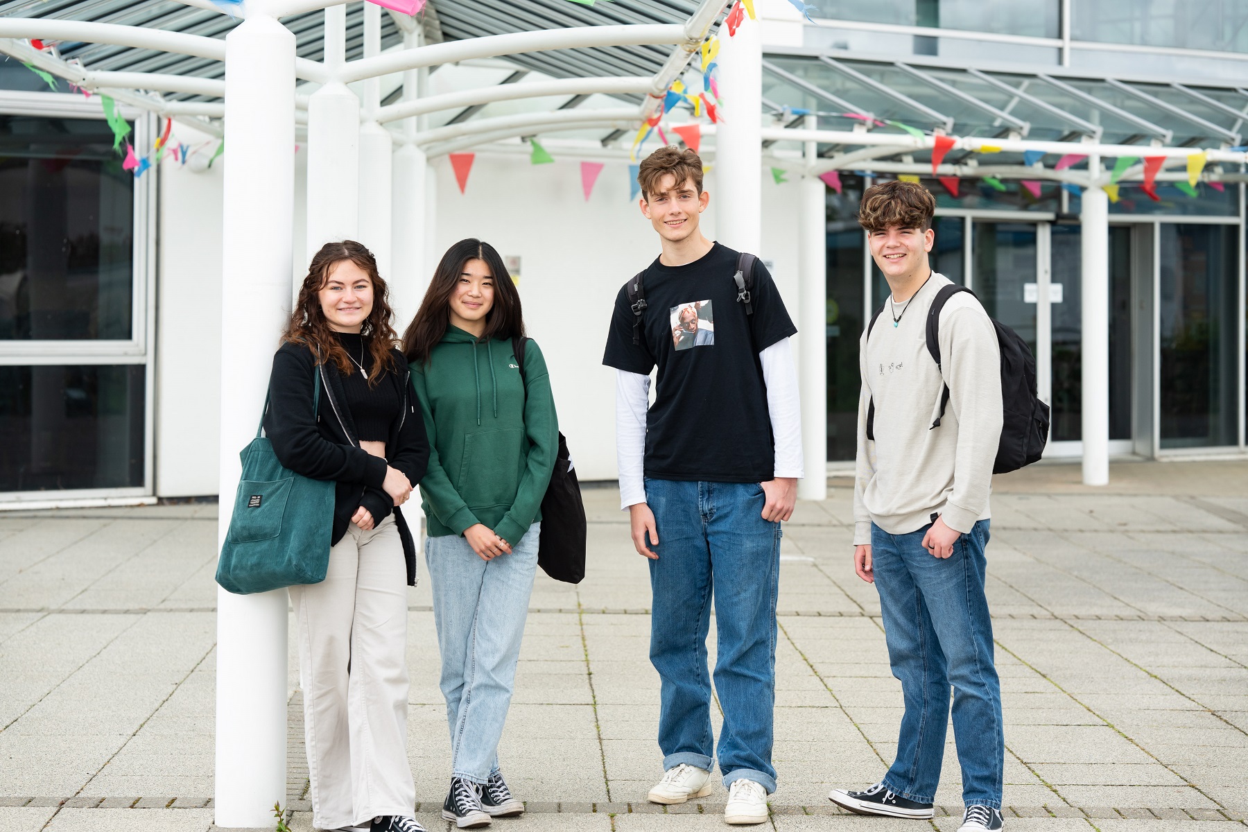 Four students stand outside the Fal building. They all look at the camera. There is bunting on the building behind them.