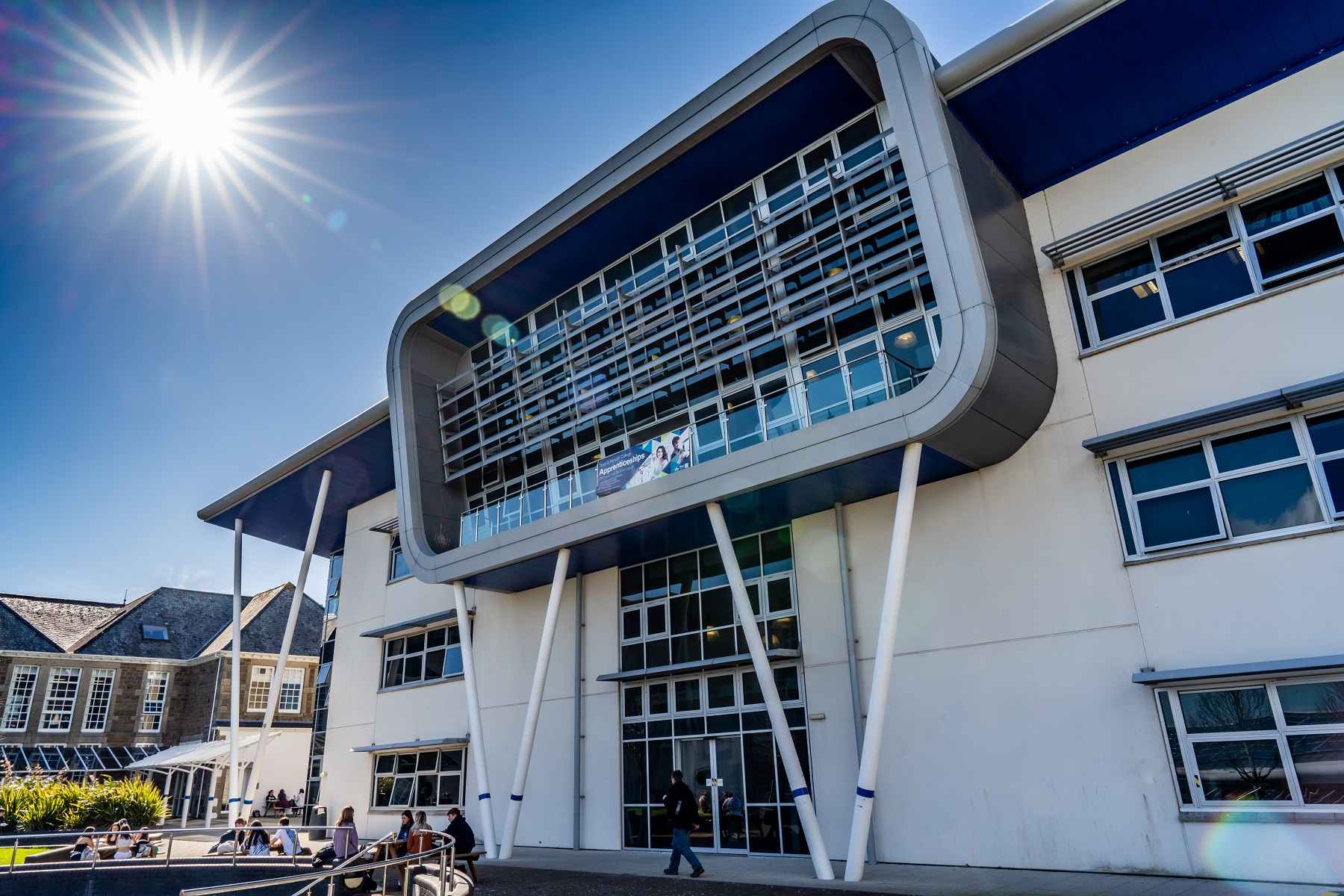 An image of the Sennen building with the sun in the top left corner as a flash. Students sit outside the building socialising.