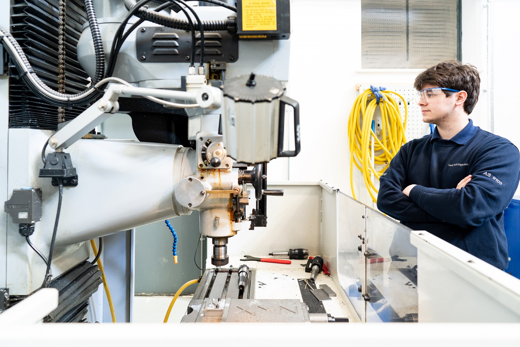A student observes equipment in the engineering bay with their arms folded.