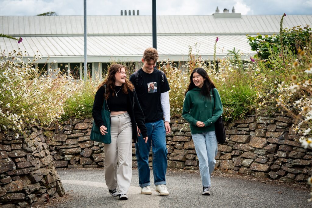 Three students walk together side by side through the grounds of Truro campus. They laugh and smile together.