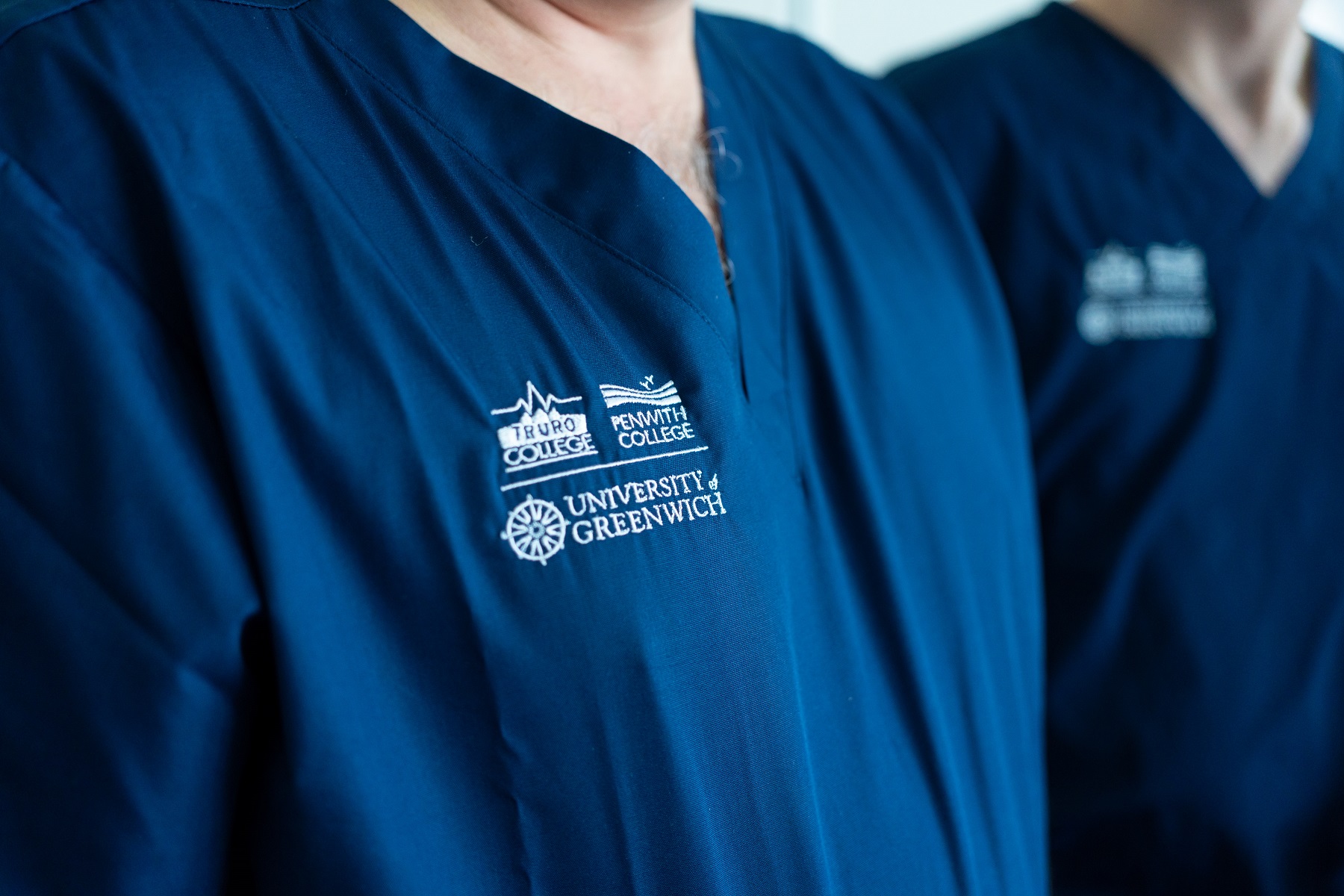 A close up image of a nursing and allied health student's scrubs. The logos are Truro and Penwith College and Greenwich University.