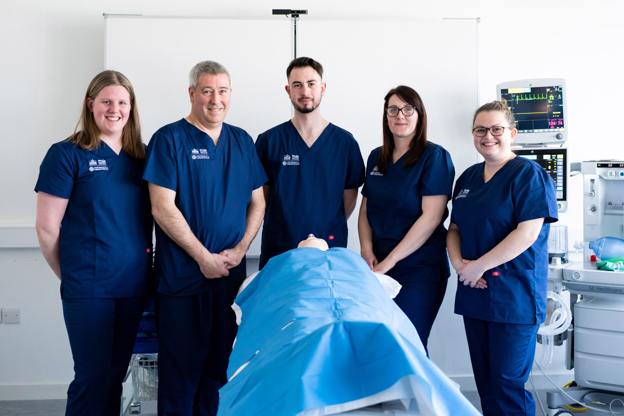 A group of operating department practitioner students smile at the camera in the simulation suite.