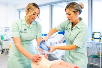 Two student nurses use a respiratory device on a practice dummy.