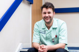 A nursing and allied health student sits in scrubs on a staircase.