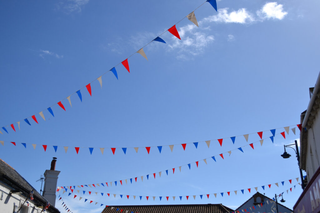 bunting hung between houses along a street against the blue sky