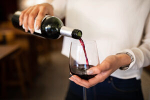 Close-up of a woman hand pouring wine into a glass. Female waiter serving red wine in a winery.