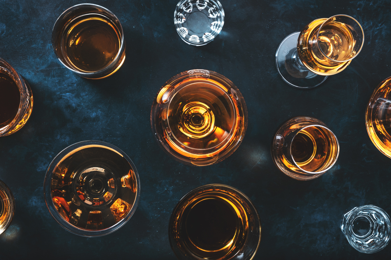 Strong alcohol drinks, hard liquors, spirits and distillates iset in glasses: cognac, scotch, whiskey and other. Blue background, top view