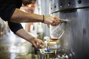 Cropped image of man filling wine from storage tank in winery