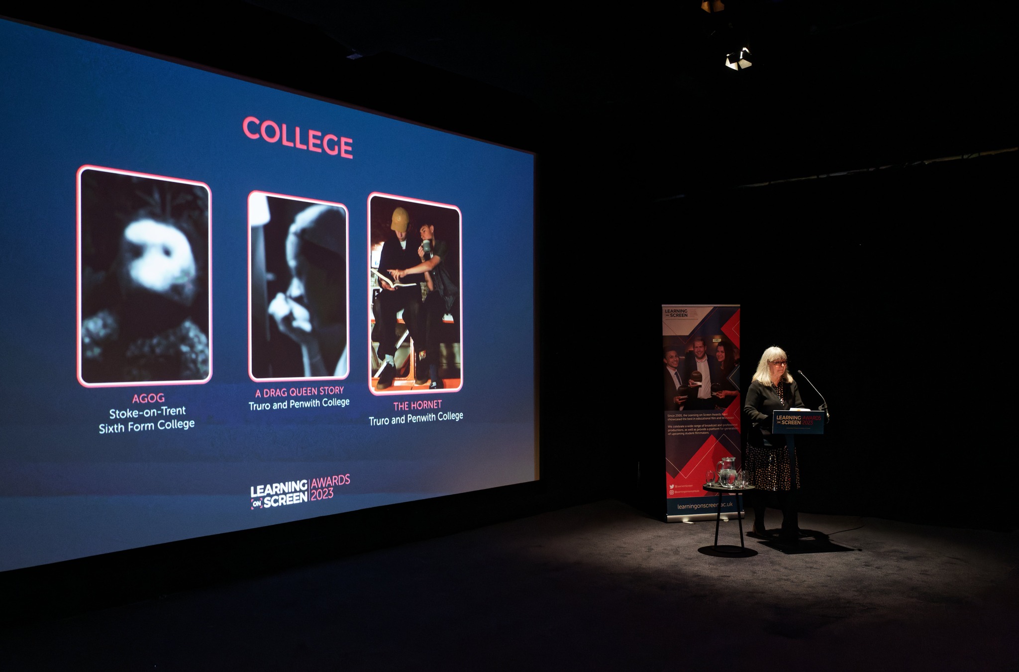 The presenter for the Learning on Screen College Award stands in front of a screen displaying 3 nominees, 2 of which are from Truro College.