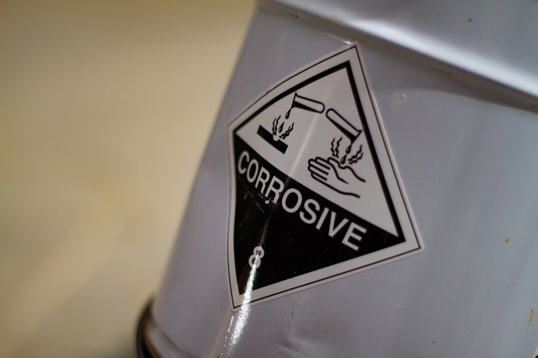 A metal bucket is labeled with a corrosive sign and text to indicate that the contents are hazardous and potentially harmful to handle.